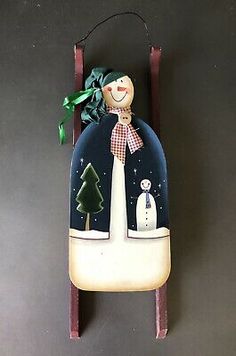 a wooden clock with a snowman and trees on the front, hanging from it's side