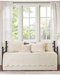 a day bed with white linens and pillows in front of a large open window