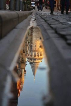 a reflection of a building in a puddle on the ground with people walking around it