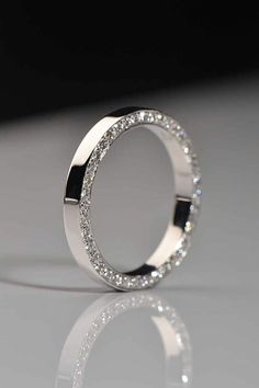 a white gold ring with round diamonds on the outside and inside, sitting on a reflective surface