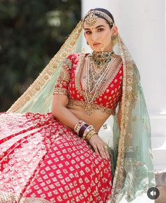 a woman in a red and gold bridal outfit sitting on a white pillar with her hand on her hip