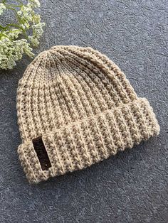 a crocheted beanie sits next to a small white flower on the ground