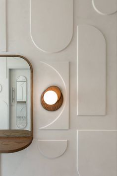 a mirror and light on the side of a white wall next to a wooden shelf