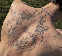 a man with tattoos on his back sitting in the grass