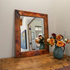 a mirror sitting on top of a wooden table next to a vase filled with flowers