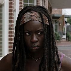 a woman with dreadlocks standing in front of a brick building and looking at the camera