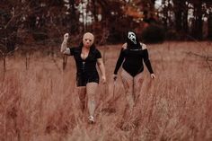 two women in bodysuits walking through tall grass with masks on their heads and hands