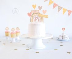 a white cake sitting on top of a table next to cupcakes and bunting