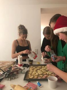 three girls in santa hats are making cookies on a table with doughnuts and milk