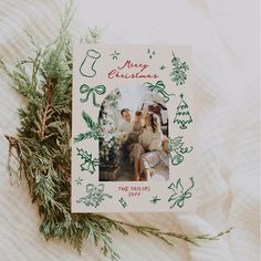 a christmas card sitting on top of a bed next to a pine tree and white blanket