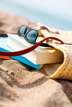 an open book, sunglasses and straw bag on the beach