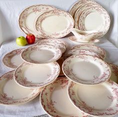 a pile of white and red china plates next to an apple on a tablecloth