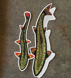 two fish stickers sitting next to each other on a cement surface in front of a wall