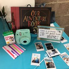 a blue table topped with pictures and polaroid cameras next to a sign that says our adventure book