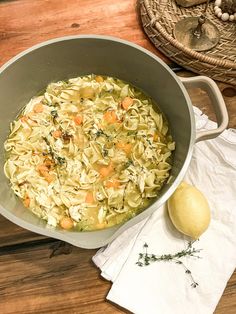 a pot filled with pasta and vegetables on top of a wooden table next to a lemon