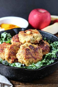 crab cakes in a cast iron skillet with lettuce and apples behind it