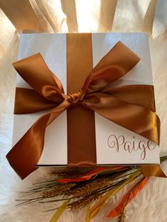 a gift box with a brown ribbon and name tag on it sitting on a white furnishing