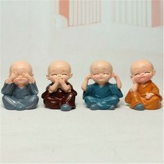 five small buddha figurines sitting in a row on a white surface, with one holding his hands to his face