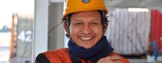 a smiling man wearing a hard hat and scarf with his hand on his chest,