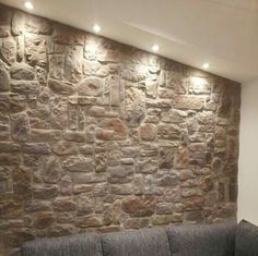 a living room with a couch and stone wall in the corner, along with recessed lighting