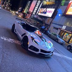 a white sports car driving down a street next to tall buildings