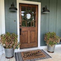 two potted plants sit on the front porch next to a welcome mat that says home sweet