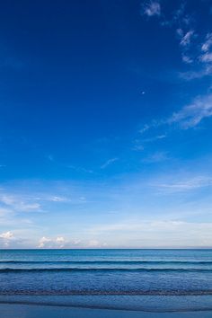 two people walking on the beach with surfboards in their hands, under a blue sky