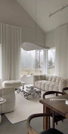 a living room filled with white furniture and large windows covered in draping curtains