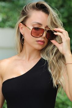 a woman wearing sunglasses and a black top is holding her hair up to her face