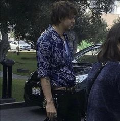 two people standing next to each other on a sidewalk with cars parked in the background