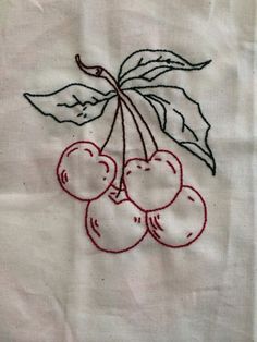 embroidered cherries with leaves on a white linen material background, showing the outline of a leaf and four cherries