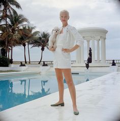 a woman standing in front of a pool holding a dog