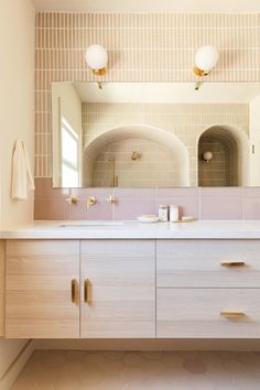 a bathroom vanity with two mirrors above it and gold pulls on the cabinet doors that are open