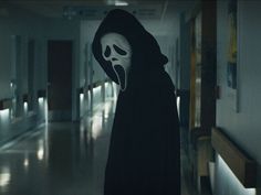 a person in a black robe with a ghost mask on walking down a hallway at night