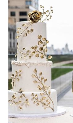 a white and gold wedding cake sitting on top of a table next to a glass of wine