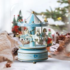 a blue carousel with white horses in front of a christmas tree and other holiday decorations