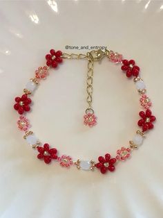 a bracelet with red flowers and white beads on a gold plated metal link chain