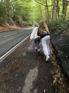 a woman is running down the road in the woods with her coat over her head