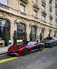 two exotic cars parked on the side of the road in front of a building with people standing outside