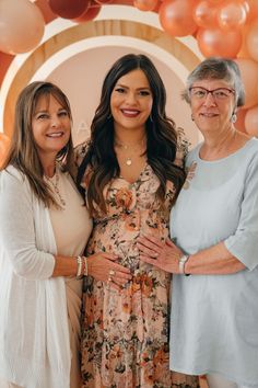 three women standing next to each other in front of an arch with balloons on it