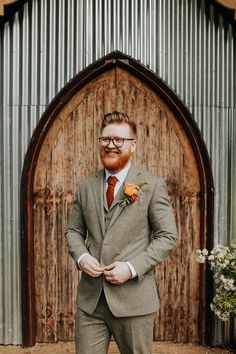 a man in a suit and tie standing next to a wooden door with an orange boutonniere