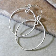 "Medium Hammered Sterling Silver Hoop Earrings, 1.75\" Diam. - Hammered Hoop Earrings - Artisan Sterling Hoop Earrings These medium sized hammered hoop earrings are created from heavy gauge sterling wire giving them a heft and depth not usually found in hoop earrings. Our signature \"loop-de-loop\" design on the top adds a simple, yet elegant, design detail while the hand hammered texture catches the light with artful subtlety. Dangling from French earwires, these bold, sterling silver hoops fac Unique Adjustable Small Hoop Earrings, Unique Hypoallergenic Hoop Jewelry, Artisan Hoop Earrings For Pierced Ears, Artisan Hoop Earrings, Unique Round Hoop Earrings For Jewelry Making, Artisan Hoop Earrings With Ear Wire For Everyday, Unique Small Hammered Hoop Earrings, Unique Hypoallergenic Metal Hoop Earrings, Unique Hand Forged Small Hoop Earrings