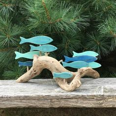 three blue metal fish on driftwood in front of pine trees