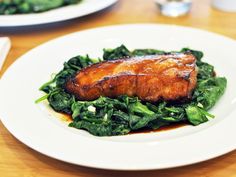 two white plates topped with meat and greens on top of a wooden table next to silverware