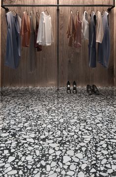 clothes are hanging on the rack in front of a wooden wall and floor with black and white designs