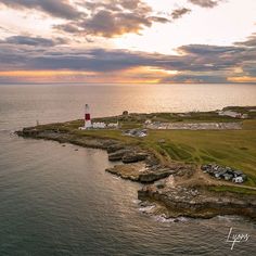 an aerial view of a lighthouse in the middle of water at sunset with clouds overhead