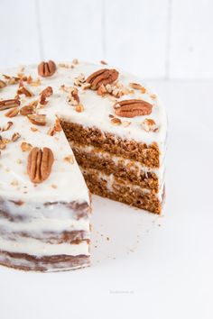 a carrot cake with white frosting and pecans on top is cut into slices