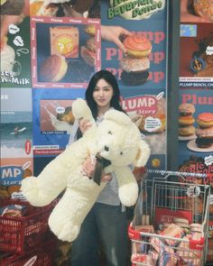 a woman holding a large white teddy bear in front of a display of doughnuts