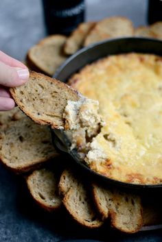 a hand holding a cracker over a bowl of dip with bread on the side