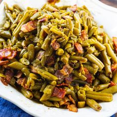 green beans with bacon on top in a white bowl sitting on a blue cloth next to a wooden table